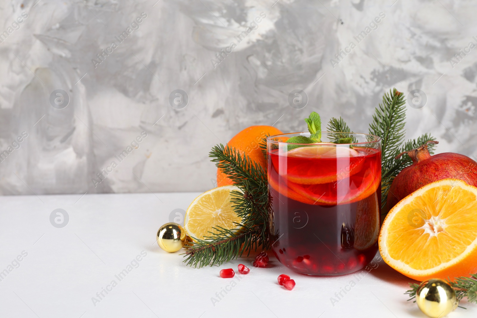 Photo of Christmas Sangria drink in glass, fir branches and fruits on white table, closeup. Space for text
