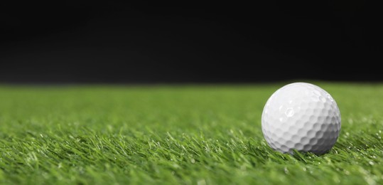 Golf ball on green grass against black background, space for text. Banner design