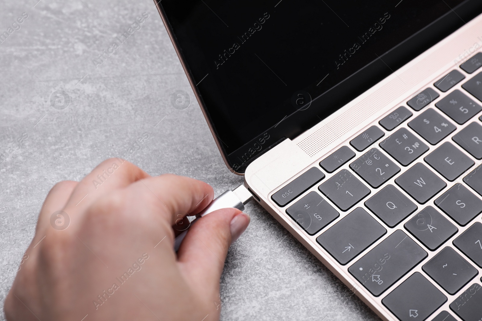 Photo of Woman plugging USB cable with type C connector into laptop port at grey table, closeup