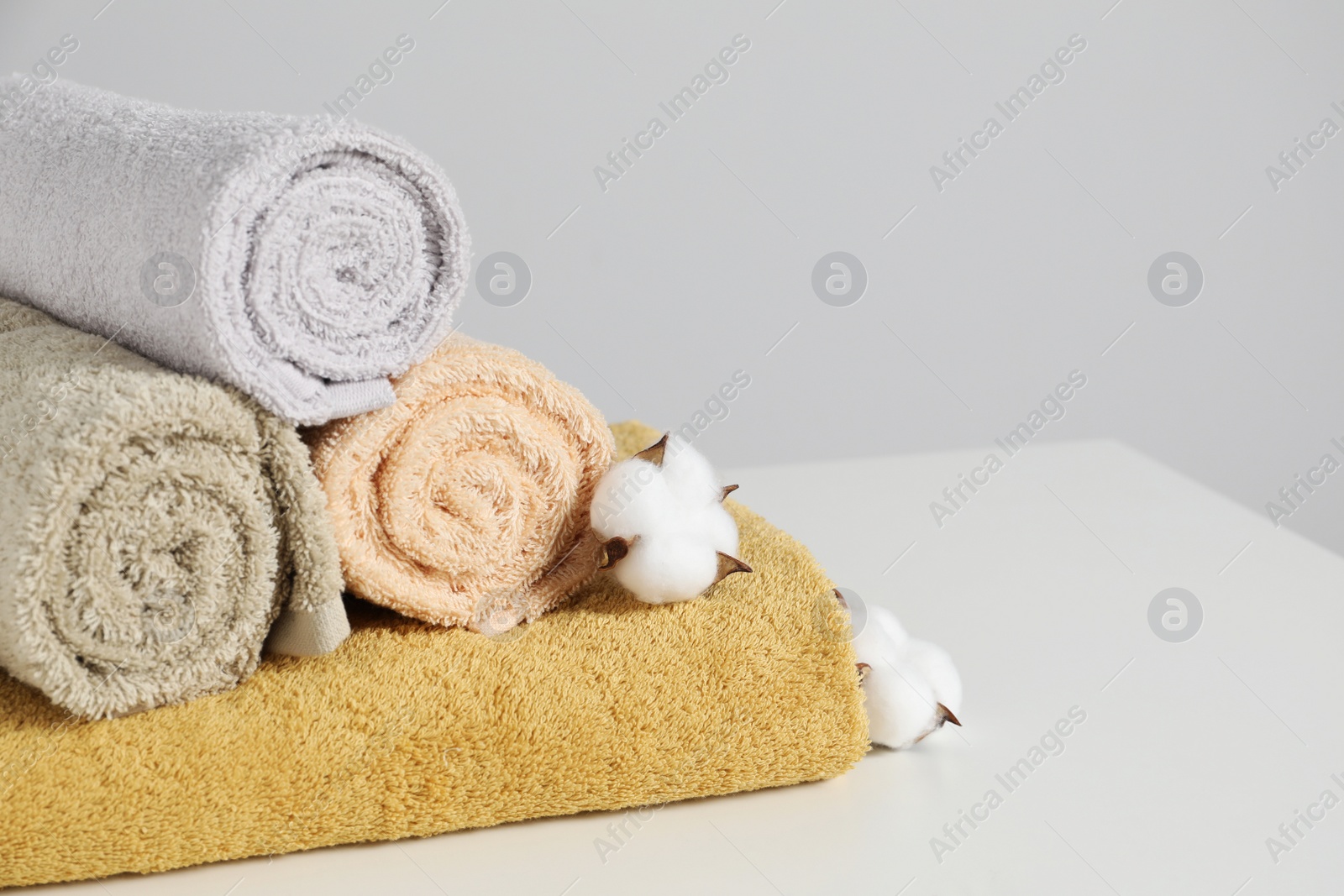 Photo of Clean soft towels with cotton flowers on white table against light grey background. Space for text