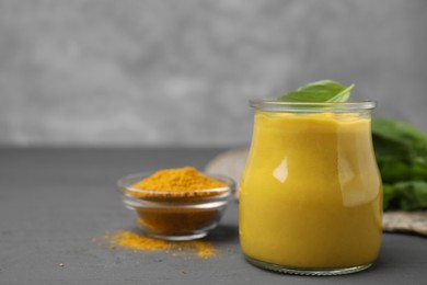 Tasty curry sauce, powder and basil leaves on grey table. Space for text