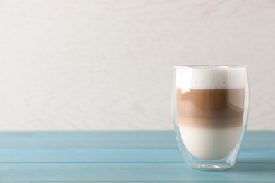 Photo of Glass of delicious layered coffee on turquoise wooden table against white background, space for text