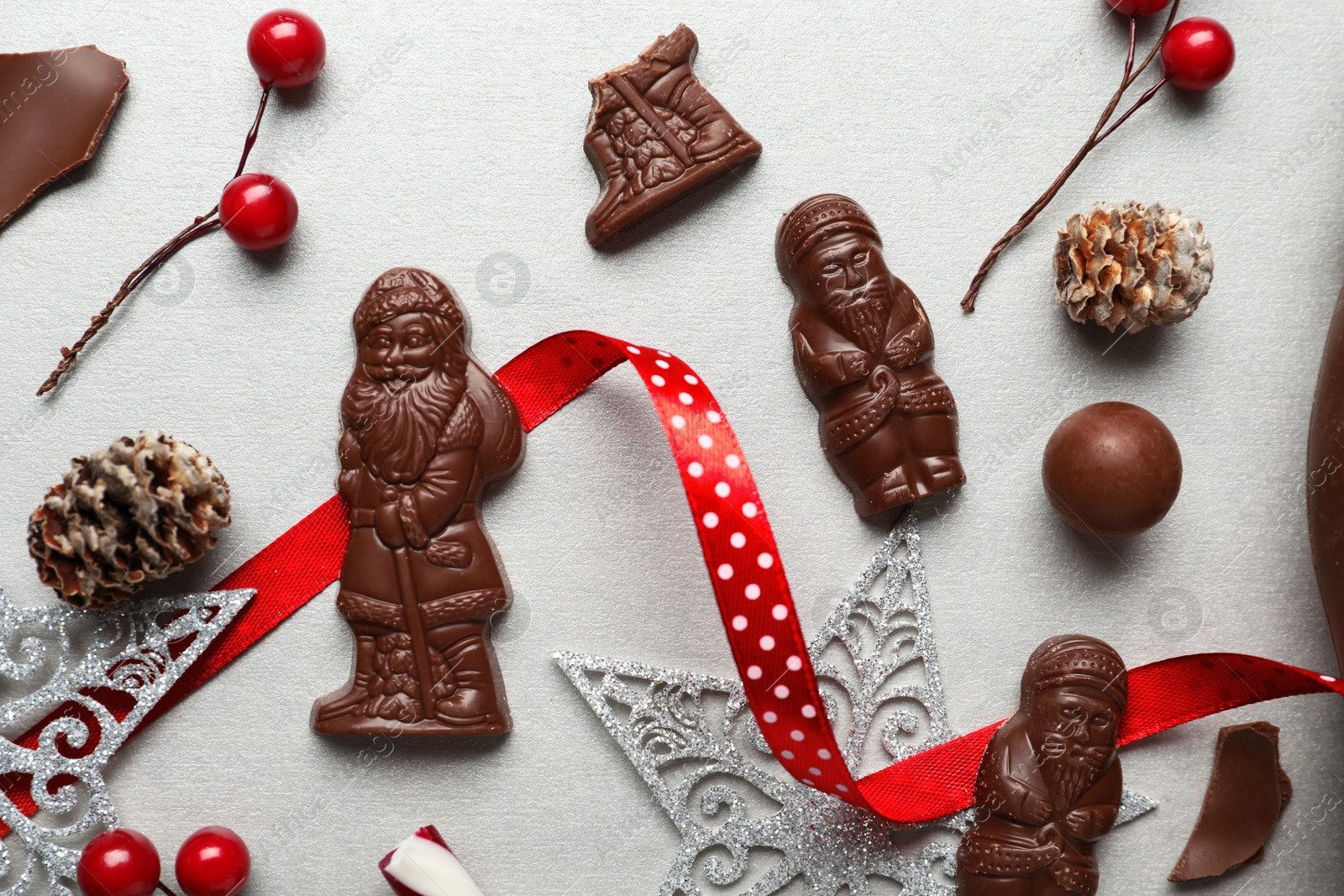 Photo of Flat lay composition with chocolate Santa Claus candies and Christmas decorations on light grey table