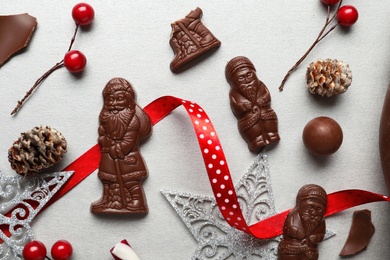 Flat lay composition with chocolate Santa Claus candies and Christmas decorations on light grey table