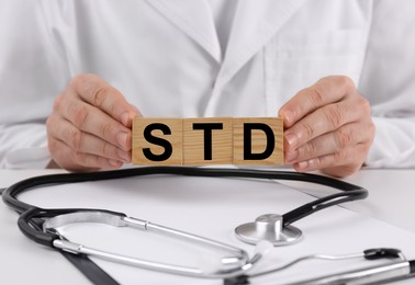Photo of Doctor holding wooden cubes with abbreviation STD at white table, closeup