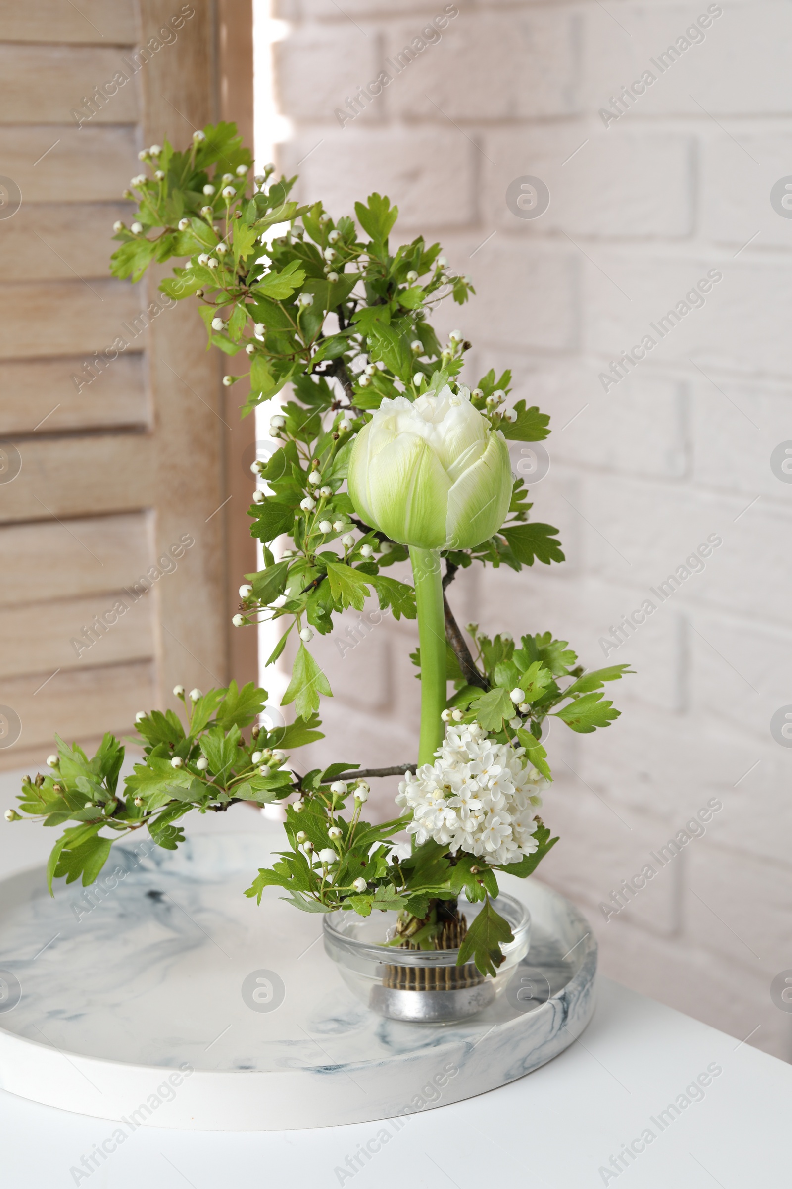 Photo of Beautiful ikebana for stylish house decor. Floral composition with fresh tulip flower and blooming branches on white table