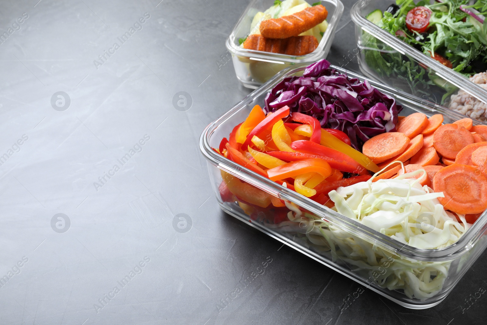 Photo of Tasty vegetables in glass container on grey table, space for text