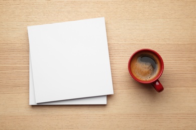 Blank paper sheets for brochure and cup of coffee on wooden background, flat lay. Mock up