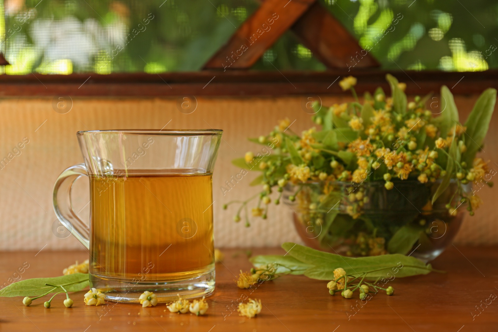 Photo of Glass cup of aromatic tea and linden blossoms on wooden table, space for text