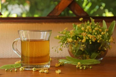Glass cup of aromatic tea and linden blossoms on wooden table, space for text