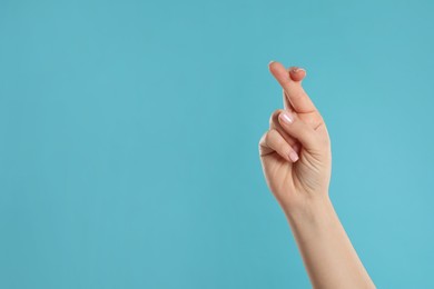 Photo of Woman holding fingers crossed on light blue background, closeup with space for text. Good luck superstition