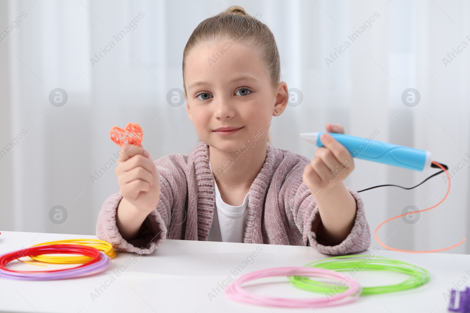 Photo of Girl drawing with stylish 3D pen at white table indoors