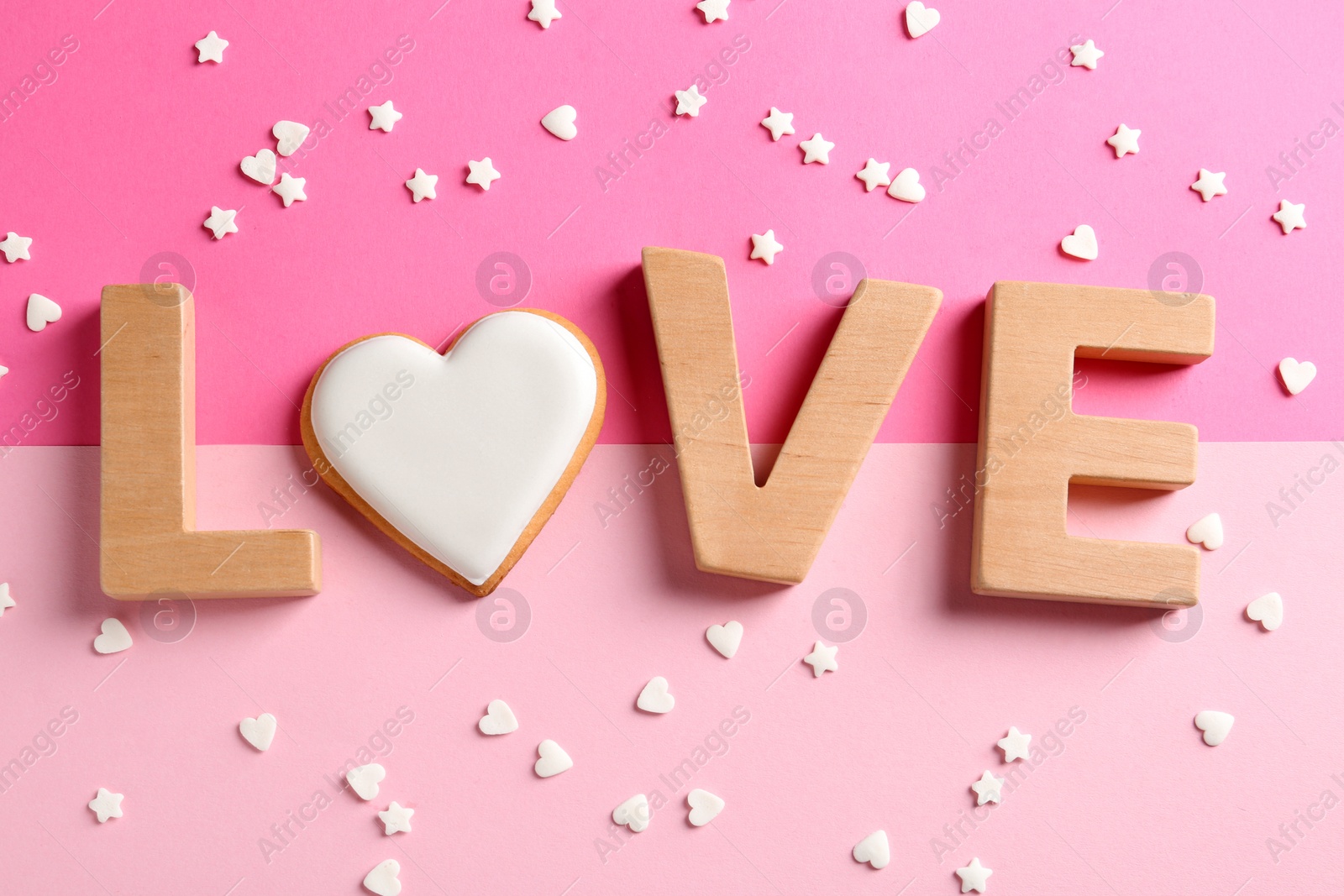 Photo of Word LOVE made with wooden letters and heart shaped cookie surrounded by candy confetti on color background, top view