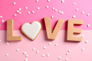 Word LOVE made with wooden letters and heart shaped cookie surrounded by candy confetti on color background, top view