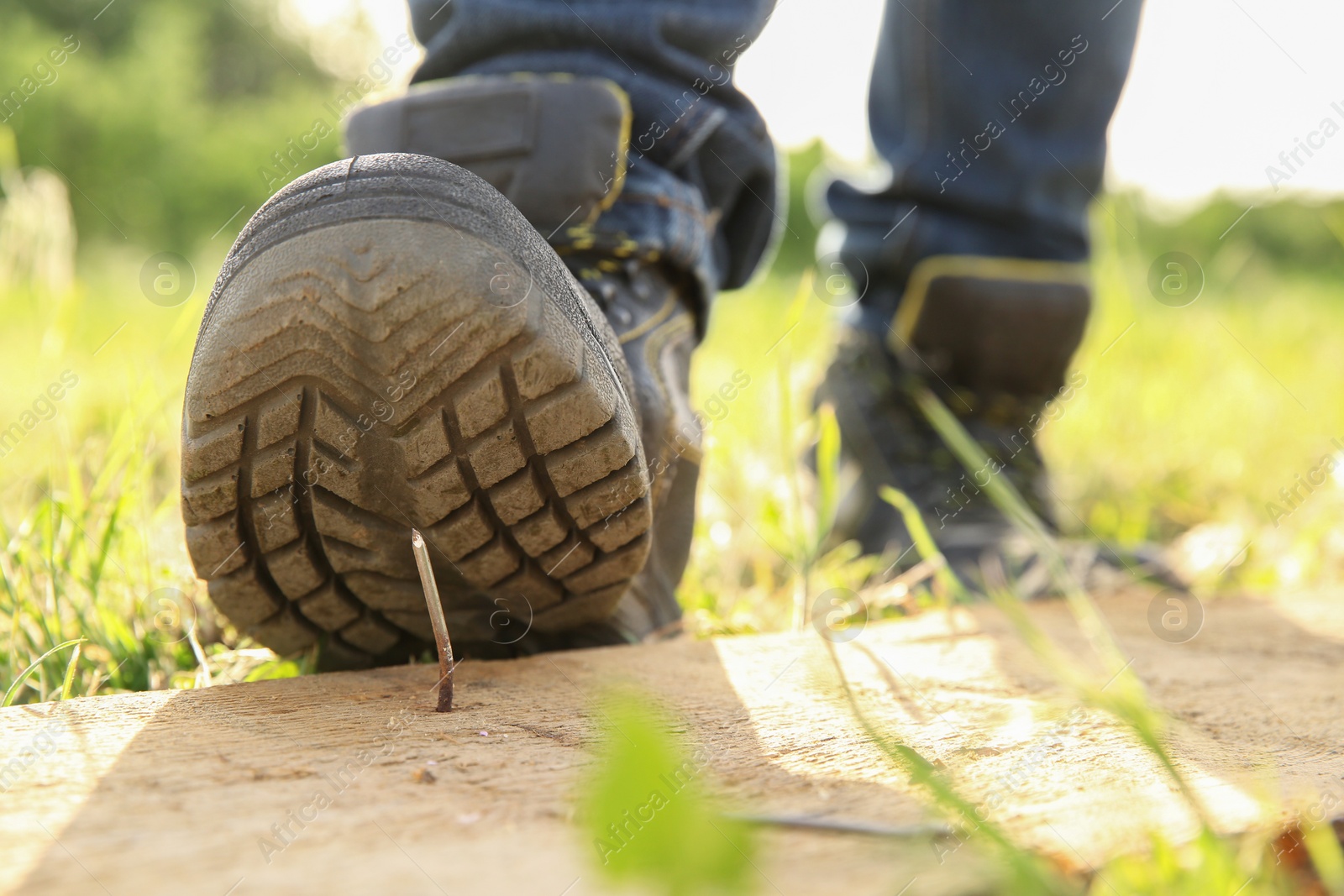 Photo of Careless worker stepping on nail in wooden plank outdoors, closeup