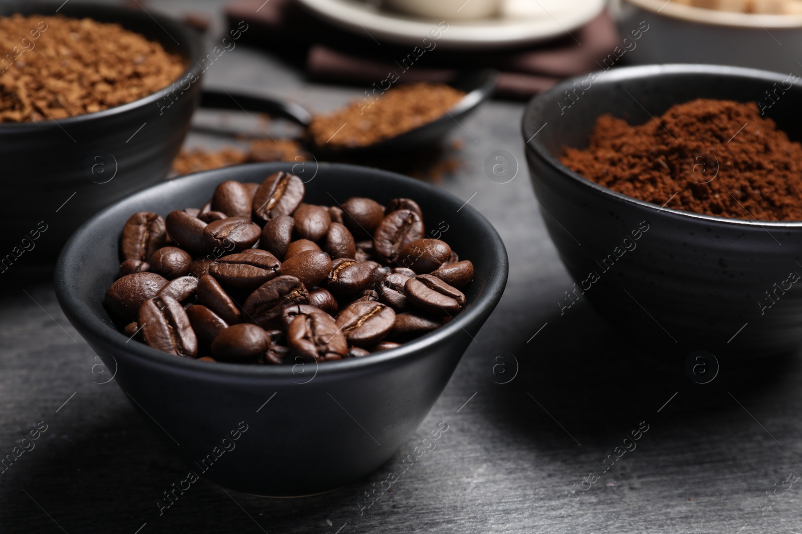 Photo of Bowls of beans, instant and ground coffee on grey table, closeup