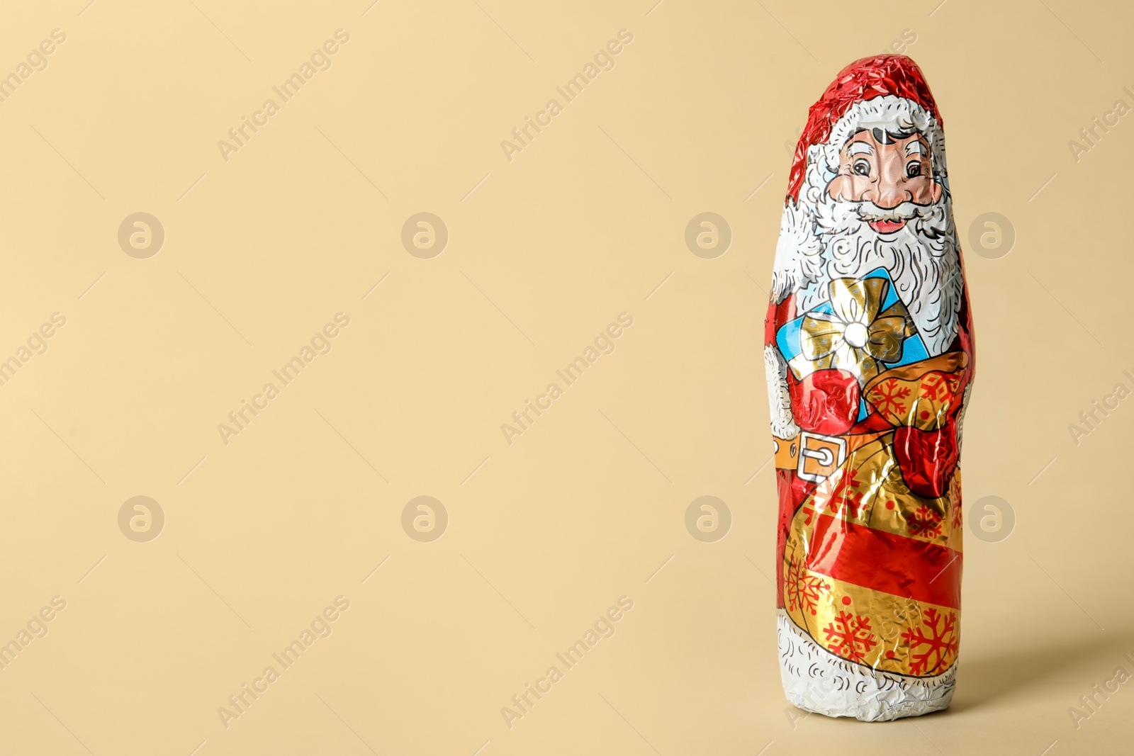 Photo of Chocolate Santa Claus in foil wrapper on beige background. Space for text