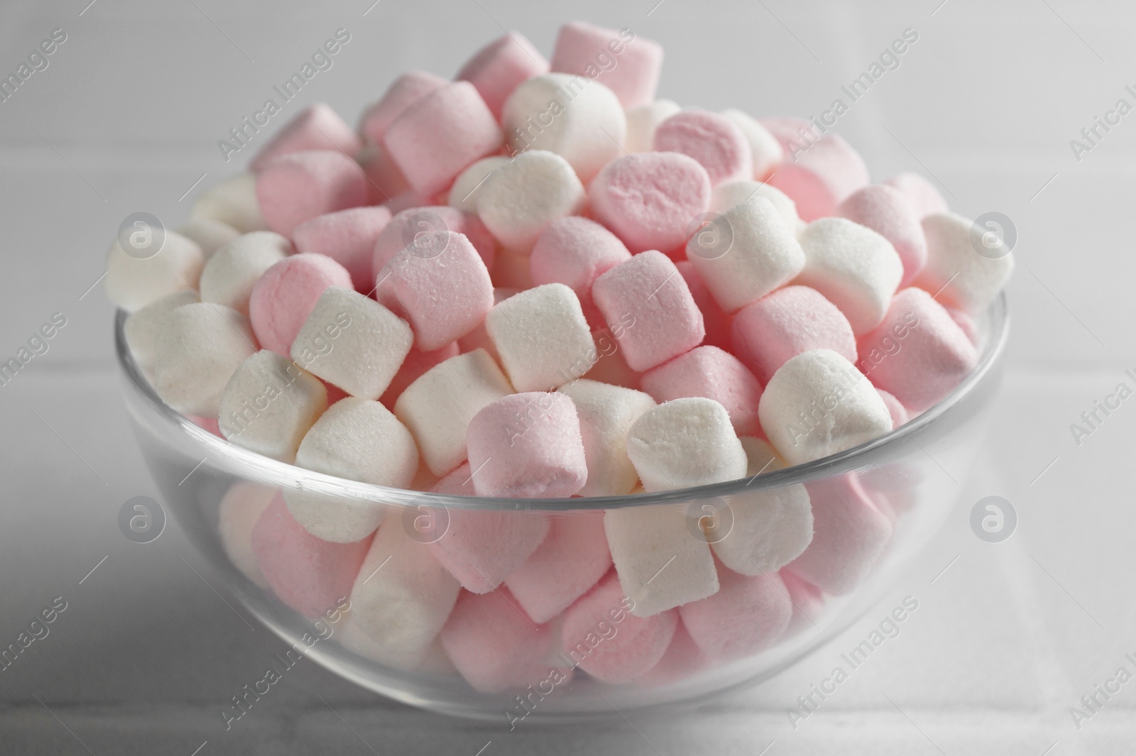 Photo of Glass bowl with delicious marshmallows on white table, closeup