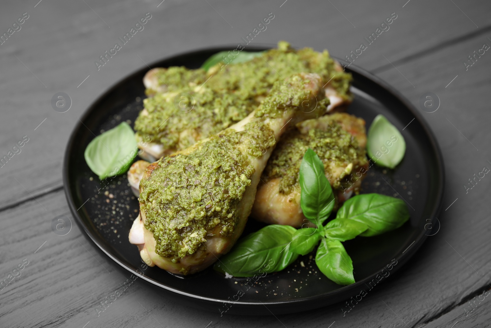 Photo of Delicious fried chicken drumsticks with pesto sauce and basil on gray wooden table, closeup