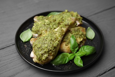Delicious fried chicken drumsticks with pesto sauce and basil on gray wooden table, closeup