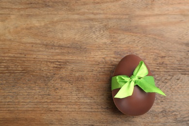 Photo of Sweet chocolate egg with green bow on wooden table, top view. Space for text