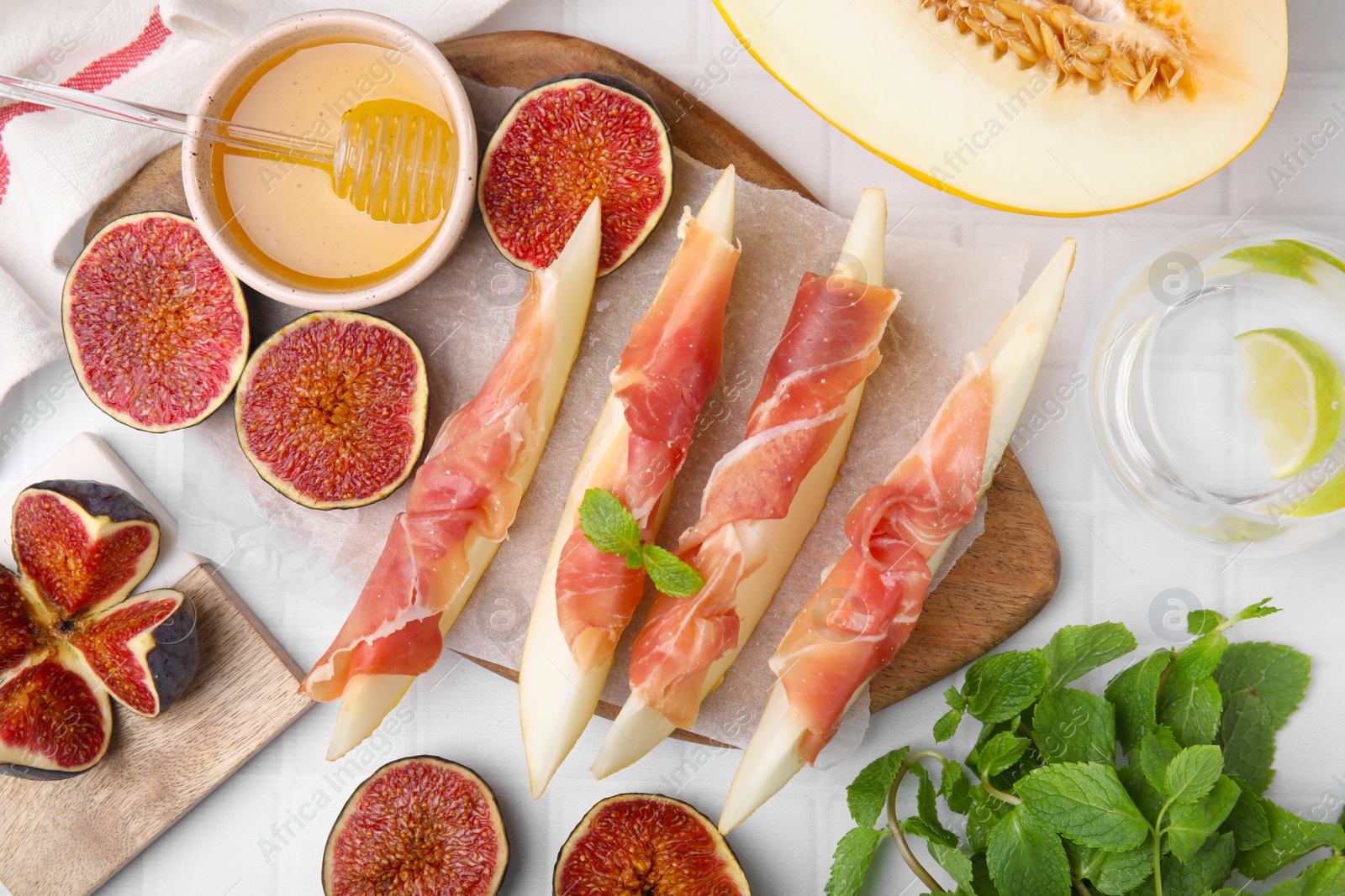 Photo of Tasty melon, jamon and figs served on white tiled table, flat lay