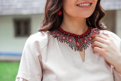 Photo of Woman wearing ornate beaded necklace in village, closeup. Ukrainian national jewelry