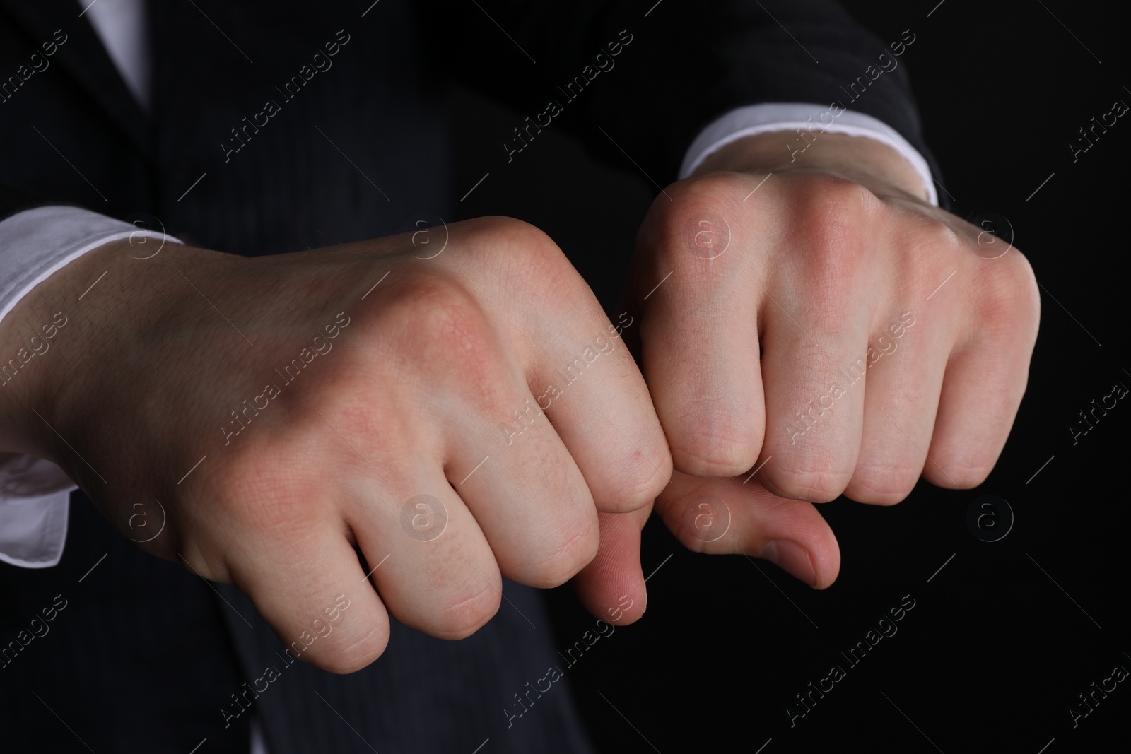 Photo of Businessman showing fists with space for tattoo on black background, closeup
