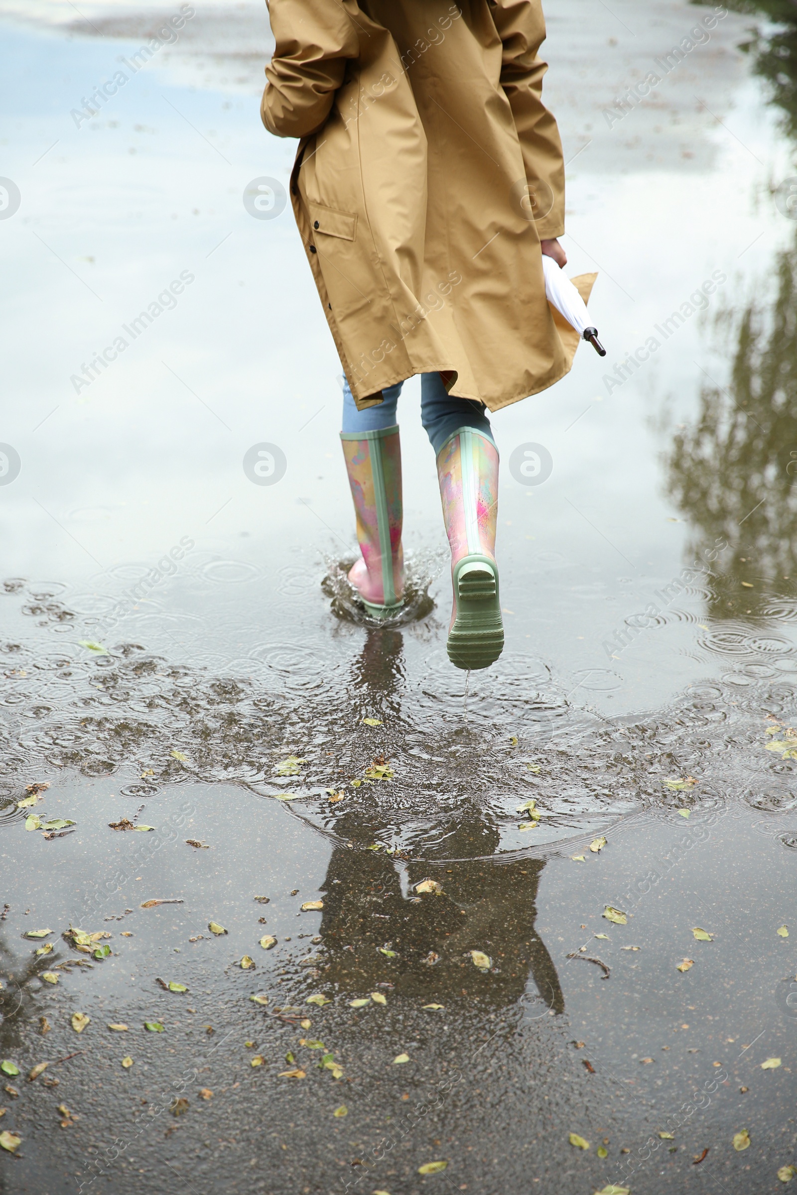 Photo of Woman with rubber boots running in puddle, closeup. Rainy weather