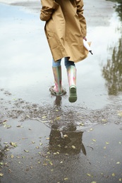 Woman with rubber boots running in puddle, closeup. Rainy weather