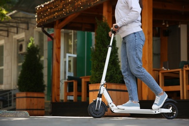 Woman riding electric kick scooter outdoors. Space for text