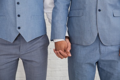 Newlywed gay couple holding hands near white wall, closeup