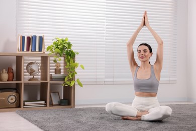 Photo of Woman in sportswear meditating at home, space for text