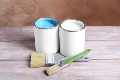 Photo of Cans of colorful paints and brushes on wooden table