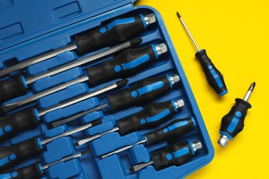 Photo of Set of screwdrivers and toolbox on yellow table, flat lay
