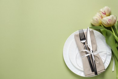 Photo of Stylish table setting with cutlery and tulips on light green background, flat lay. Space for text