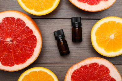 Bottles of citrus essential oils and fresh fruits on wooden table, flat lay
