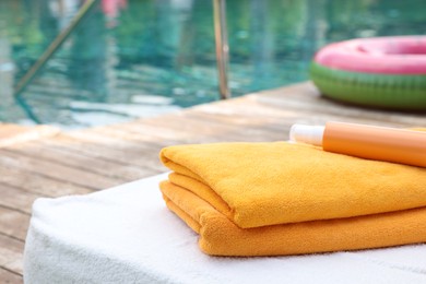 Photo of Beach towels and sunscreen on sun lounger near outdoor swimming pool at luxury resort, selective focus. Space for text