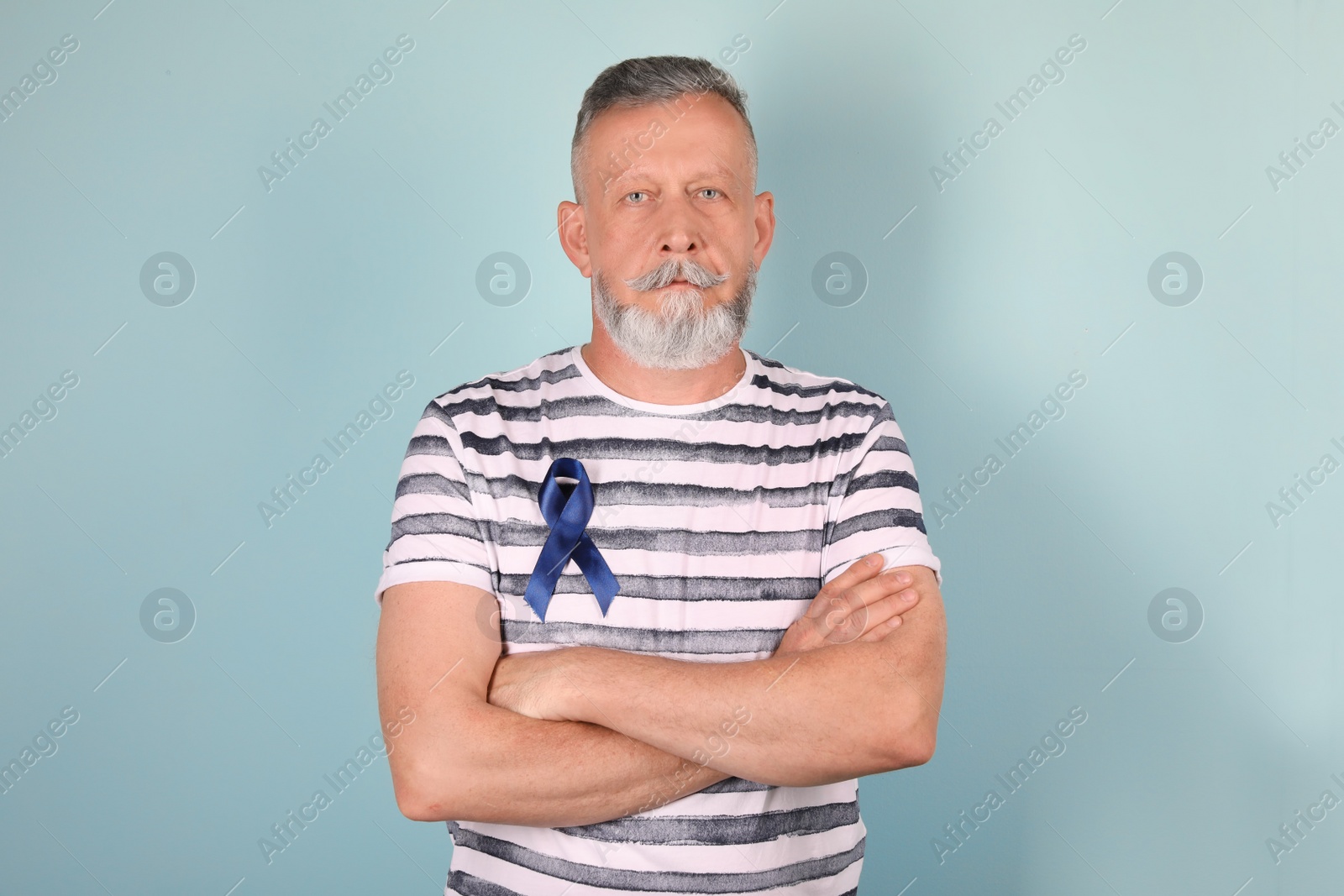 Photo of Mature man with blue ribbon on color background. Urological cancer awareness