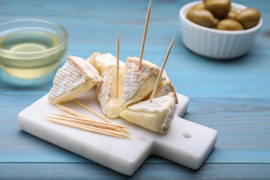 Photo of Toothpick appetizers. Pieces of camembert on light blue wooden table