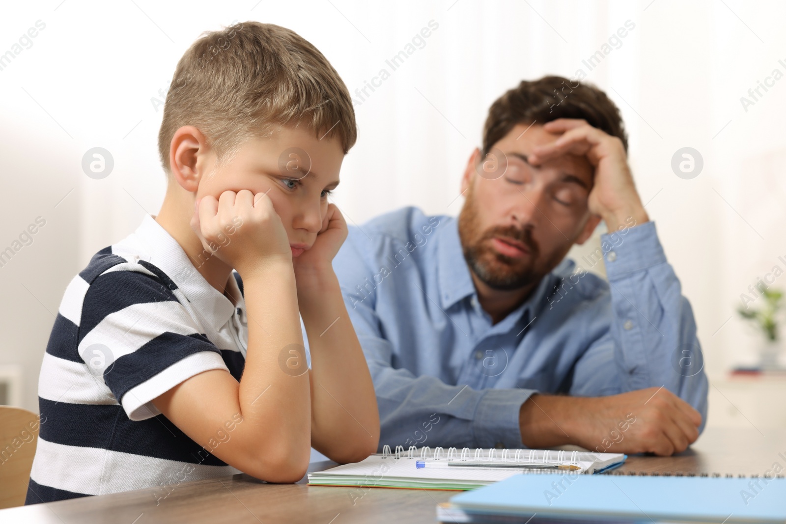 Photo of Dyslexia problem. Annoyed father helping son with homework at table indoors, selective focus