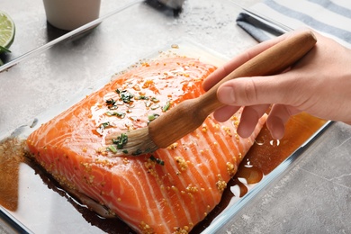 Photo of Woman marinating raw salmon in dish at table