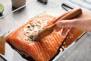 Woman marinating raw salmon in dish at table