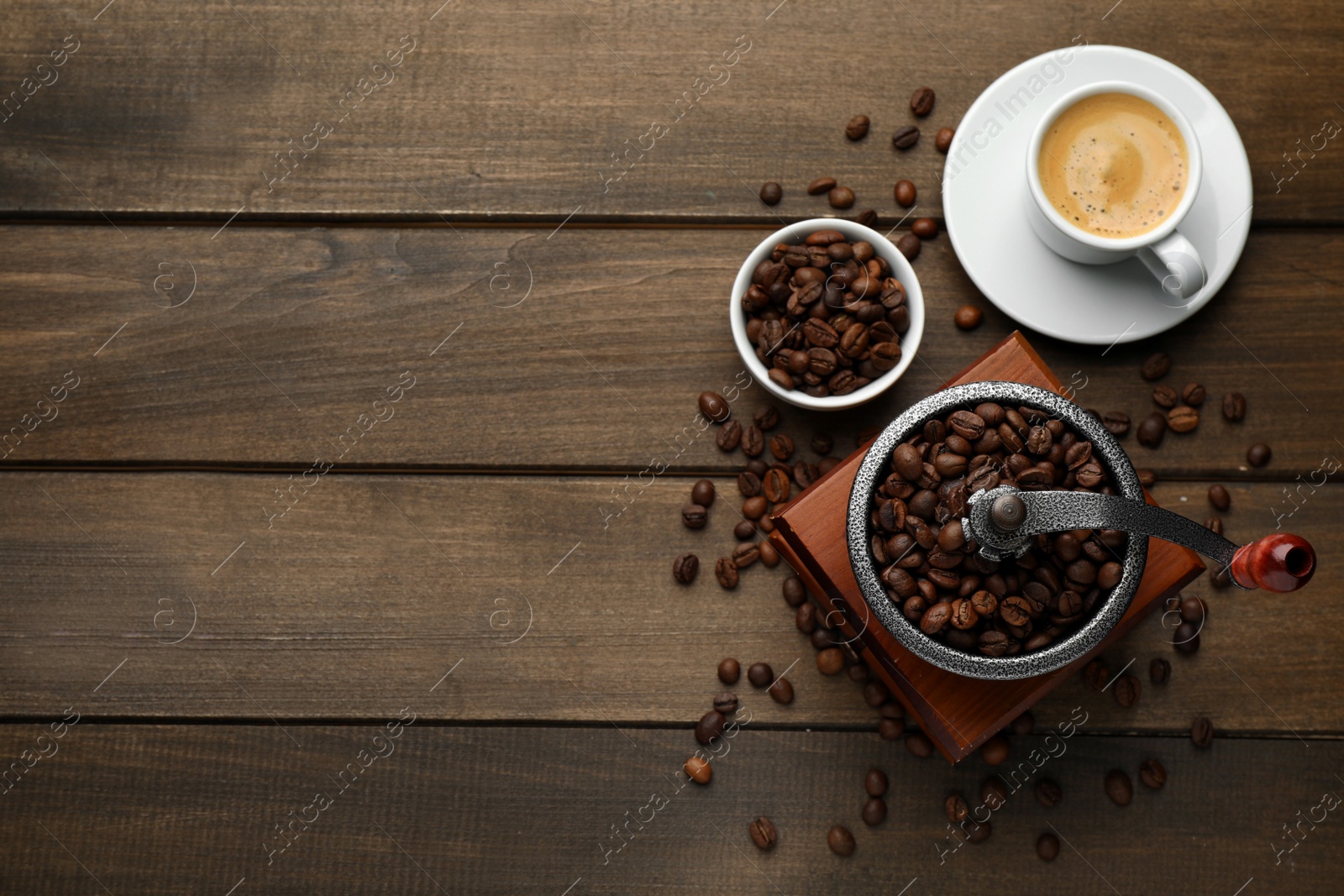 Photo of Vintage manual coffee grinder with beans and cup of drink on wooden table, flat lay. Space for text