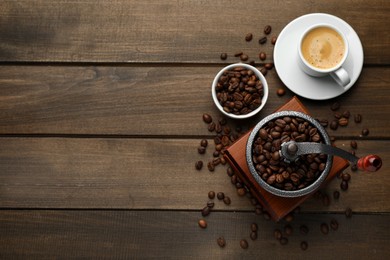 Photo of Vintage manual coffee grinder with beans and cup of drink on wooden table, flat lay. Space for text