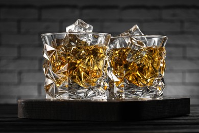 Photo of Whiskey and ice cubes in glasses on black wooden table, closeup