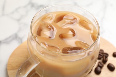 Refreshing iced coffee with milk in glass cup on white table, closeup