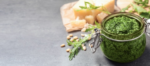 Jar of arugula pesto and ingredients on grey table, space for text. Banner design 