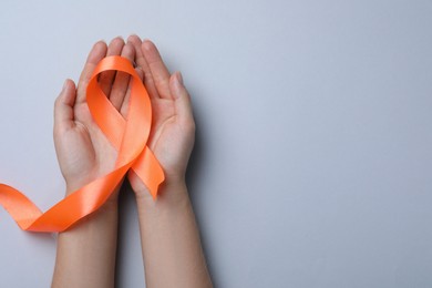 Photo of Woman holding orange ribbon on light grey background, top view with space for text. Multiple sclerosis awareness