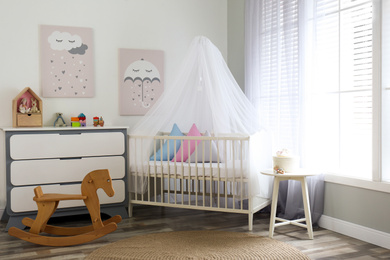 Photo of Baby room interior with cute posters, chest of drawers and comfortable crib